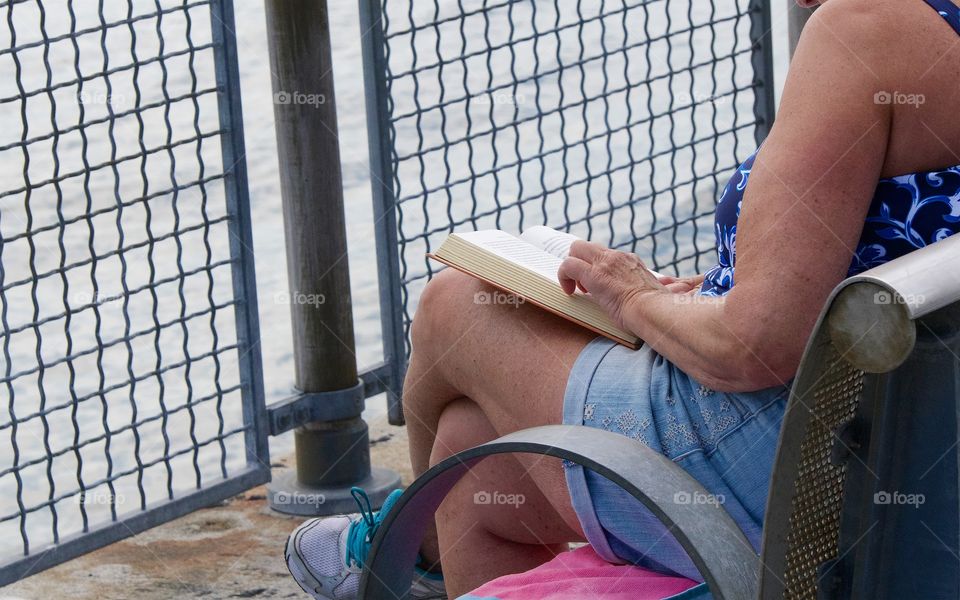 A woman leisurely reading a book in a public park facing the East River in Manhattan, New York City.