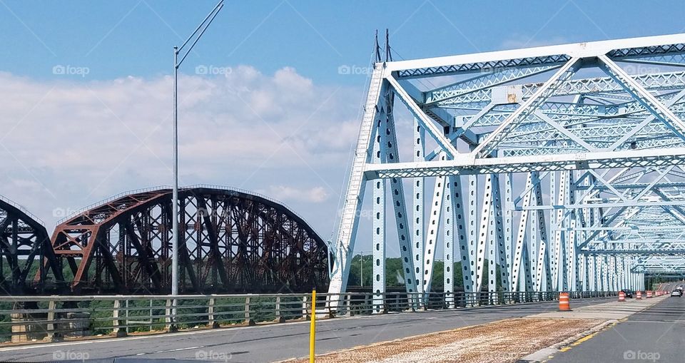 Train bridge over river along side highway traffic bridge. One old & rusted; the other new & shiny!
