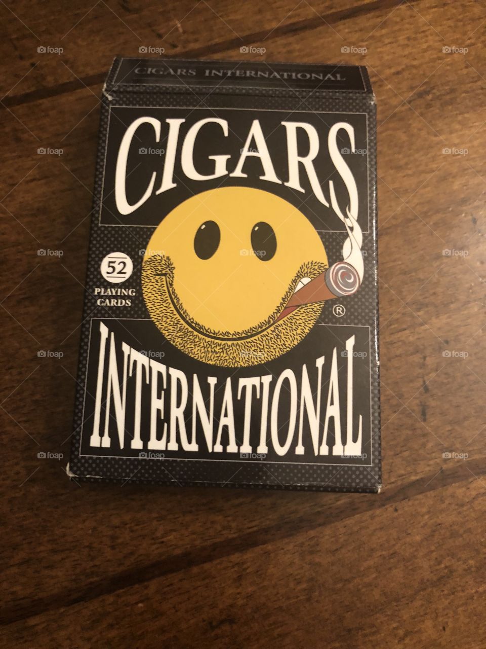 Cardboard playing card box with a smiley face on it and the words, Cigars International. 