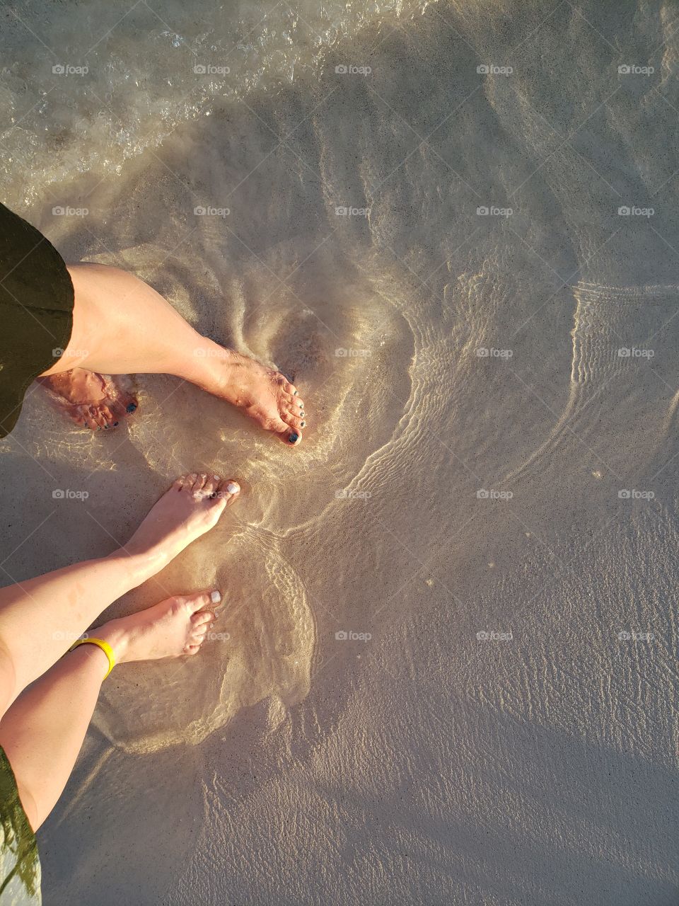 View from above, looking down at feet in sand with ocean tide ripples. Sunset glow on mother and daughter feet in sand, on vacation in Mexico.