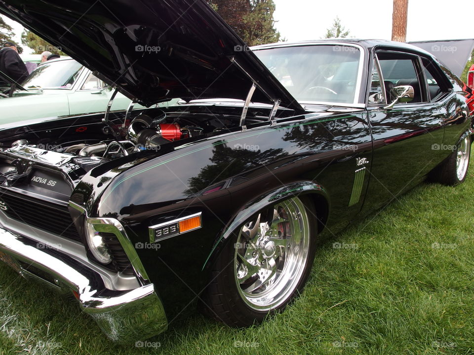 A classic bright black Chevy Nova with a raised hood at the annual car show in Drake Park in Central Oregon during the summer. 