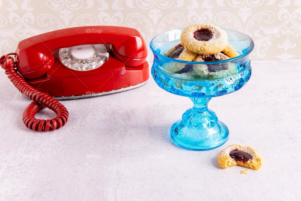 Vintage red rotary telephone next to a vintage bowl of cookies 