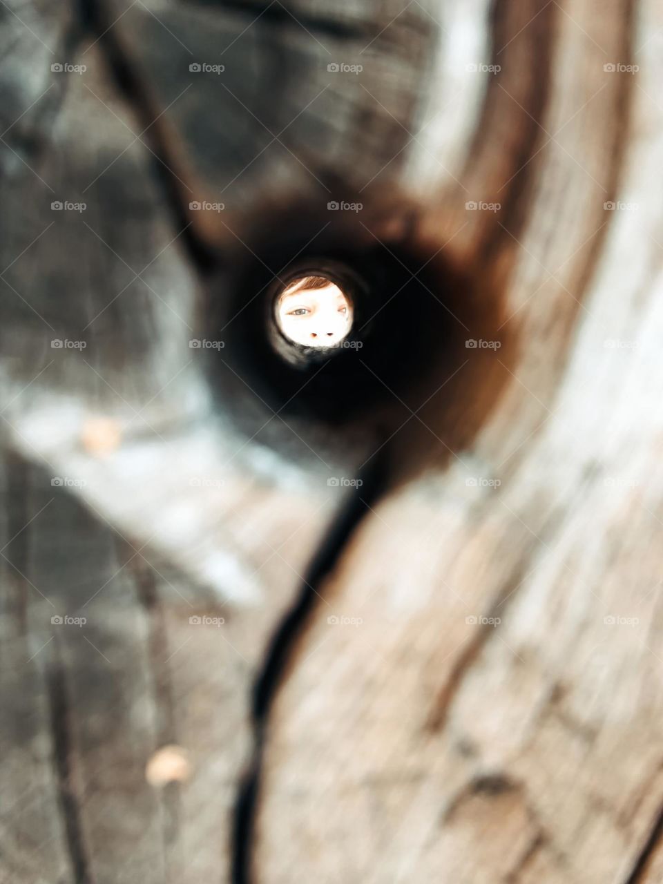 Close up of a hole in a wooden beam with a face at the other side