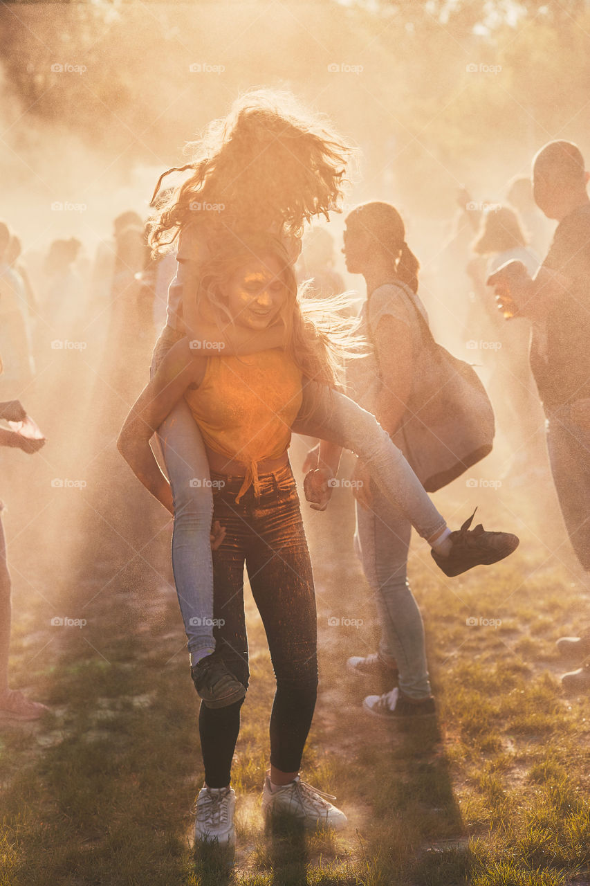 Portrait of happy smiling young girls with colorful paints on faces and clothes. Two friends spending time on holi color festival. Real people, authentic situations