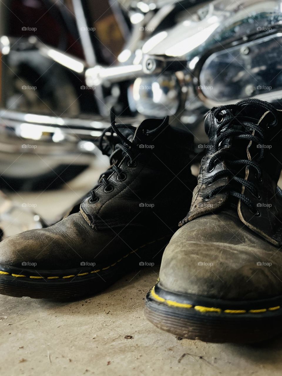 Closeup of worn, older Doc Marten classic boots with motorcycle in background 