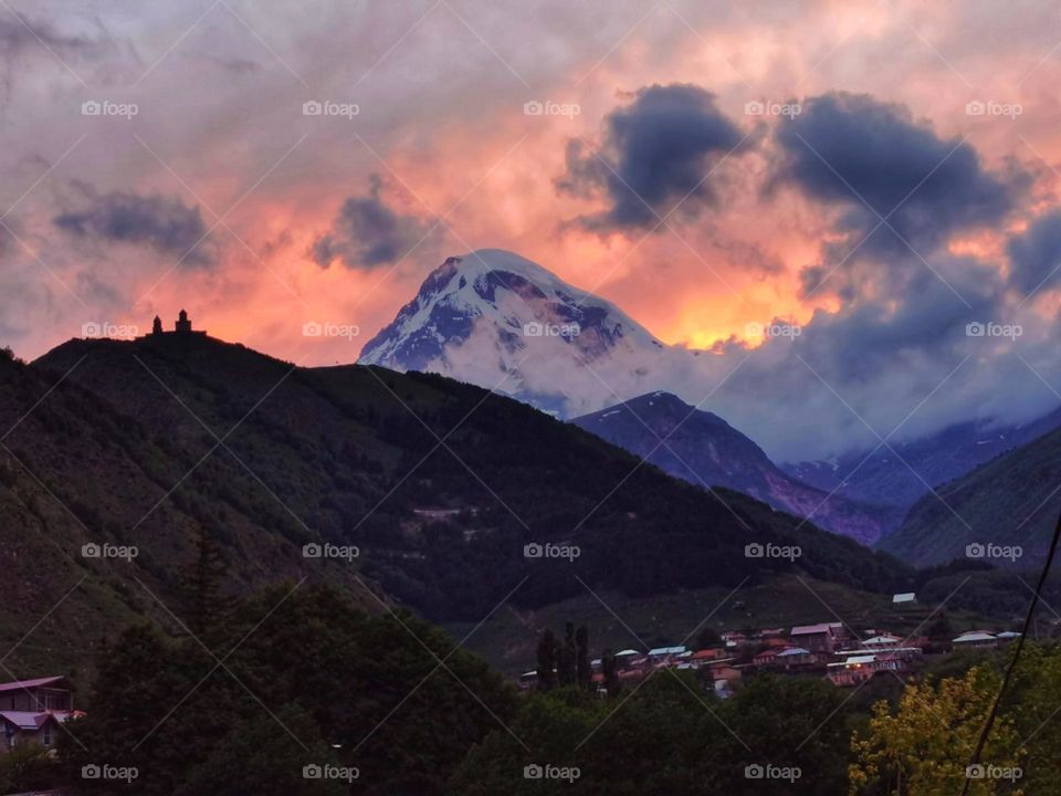 Dusk. Sunsets behind the mountain in Georgia. Cascading golden orange rays illuminates the sky.