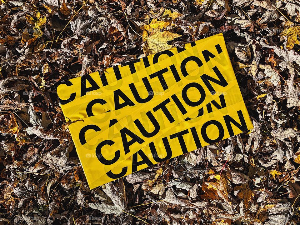 Yellow caution sign surrounded by yellow leaves, pile of autumn leaves, yellow color everywhere, yellow as a cautionary color, bright yellow, construction yellow, construction signs, yellow in the outdoors 