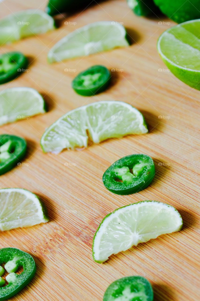 Angled view of lime and jalapeño slices on a bamboo cutting board