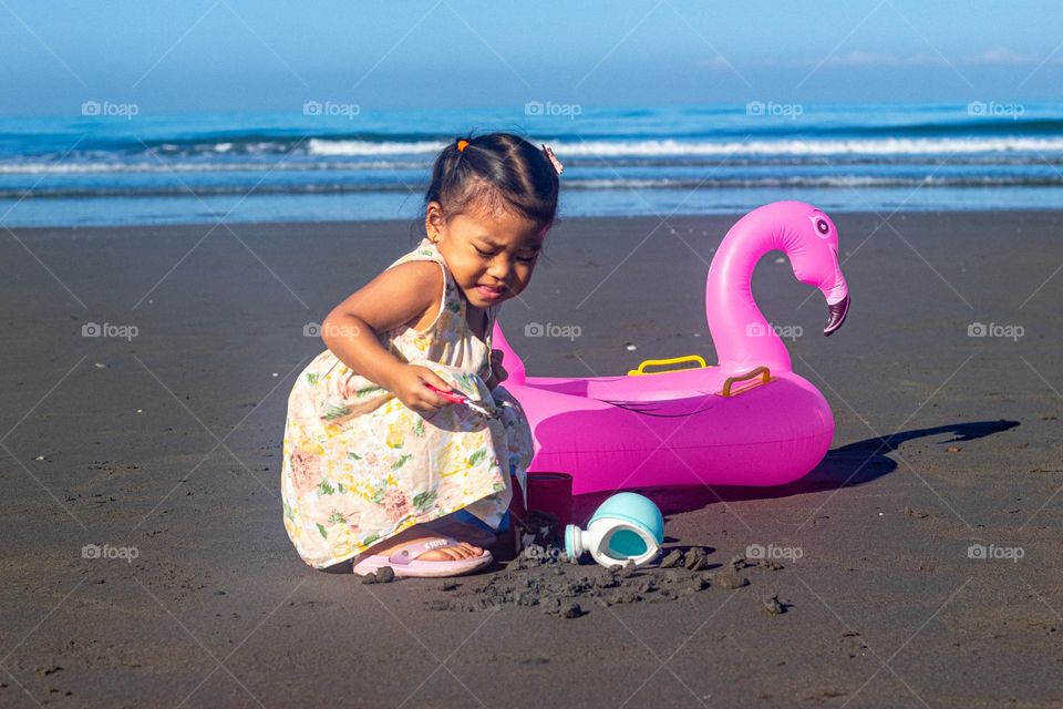 little girl playing in the sand with an inflatable under the sun