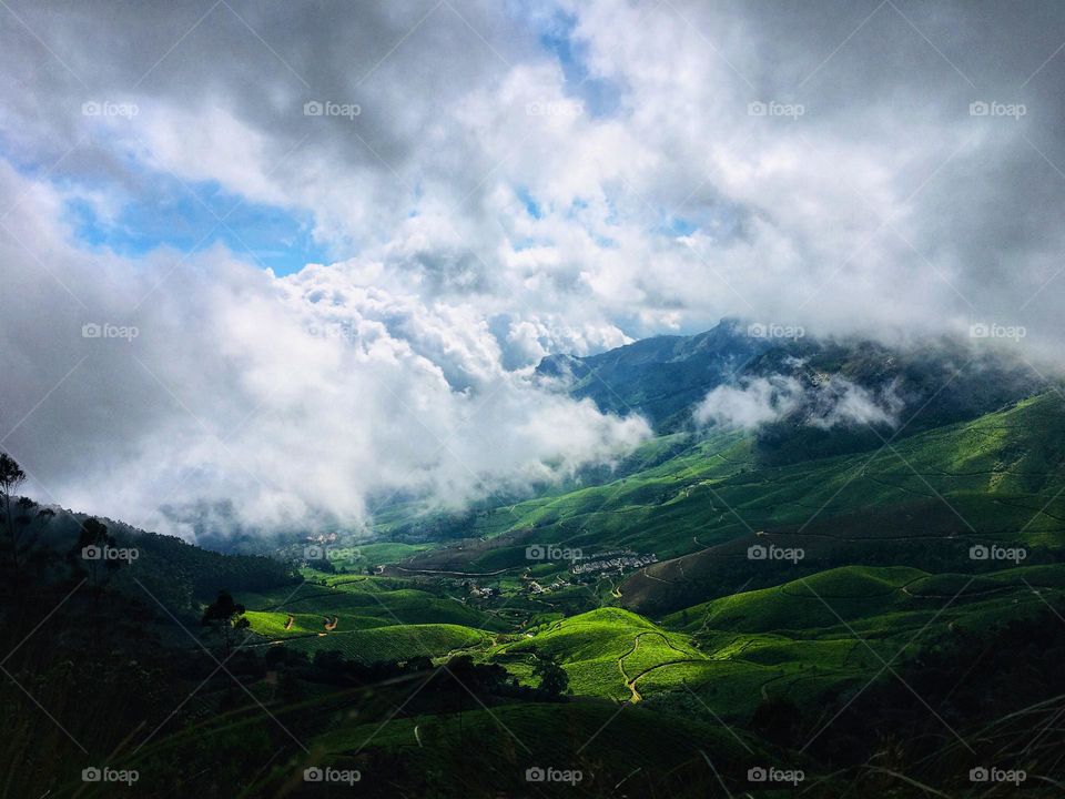 Clouds moving away to reveal a beautiful green valley hidden underneath. The lush green hills contrasted with the snow white cloud gives it an aesthetic view. 