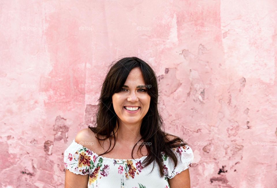 Beautiful happy young woman with dark hair standing in front of pink wall