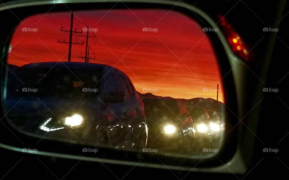 Red sunset in the driver's mirror. Headlights from the cars stuck in traffic at sundown.