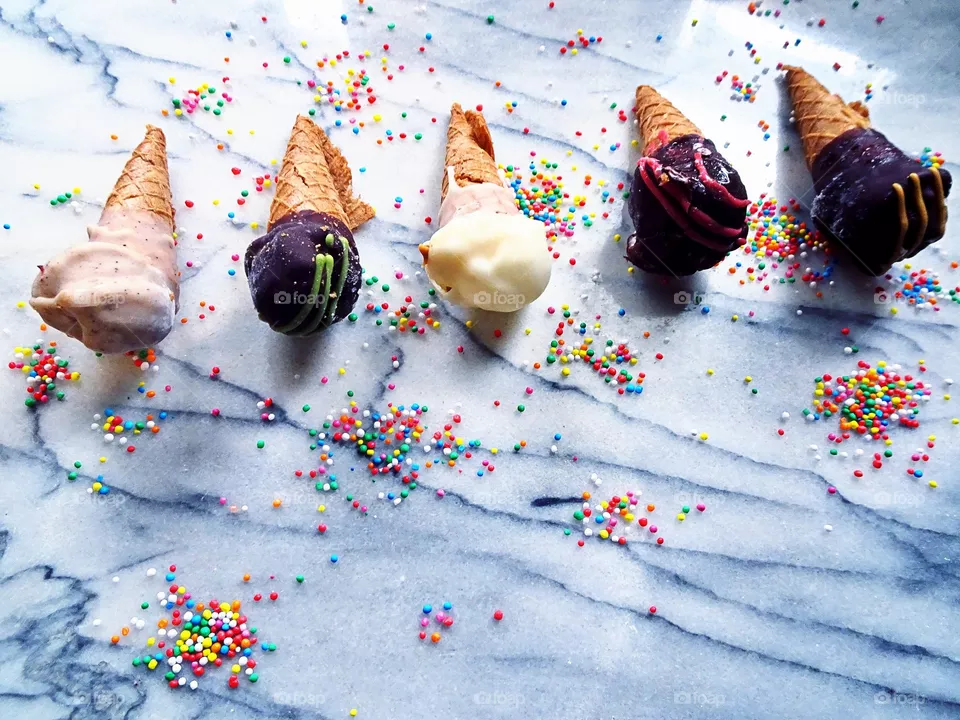 Summer frozen treats- five upside down ice cream cones on a marble table with colourful sprinkles. Minimalist, colourful flat lay overhead shot, copy space