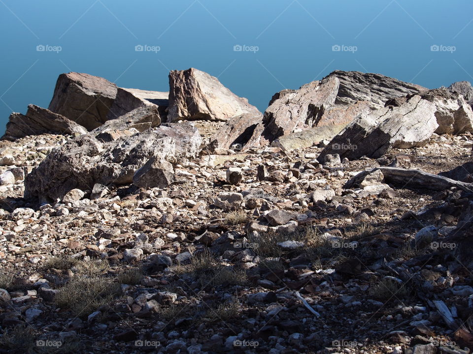 Jagged rocks and boulders along the shoreline of Ochoco Lake in Central Oregon on a sunny spring day.