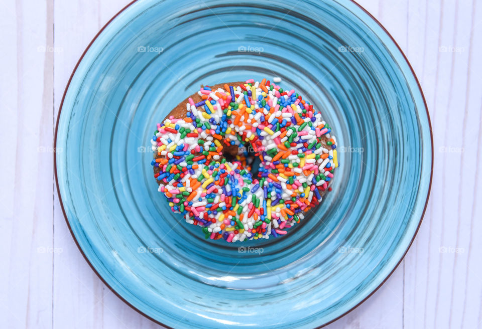 Flat lay of a rainbow sprinkles donut on a bright blue plate