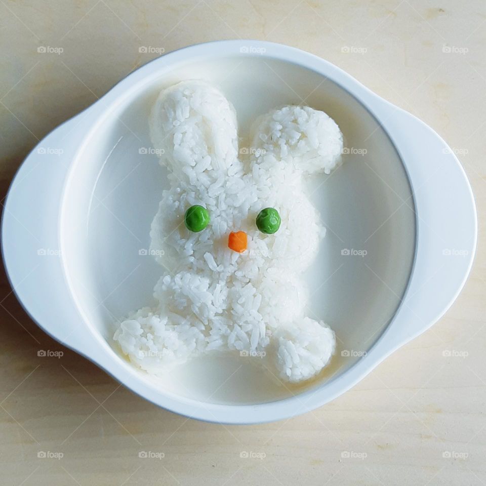 Cute bunny shape of rice on white plate against on wooden background, top view