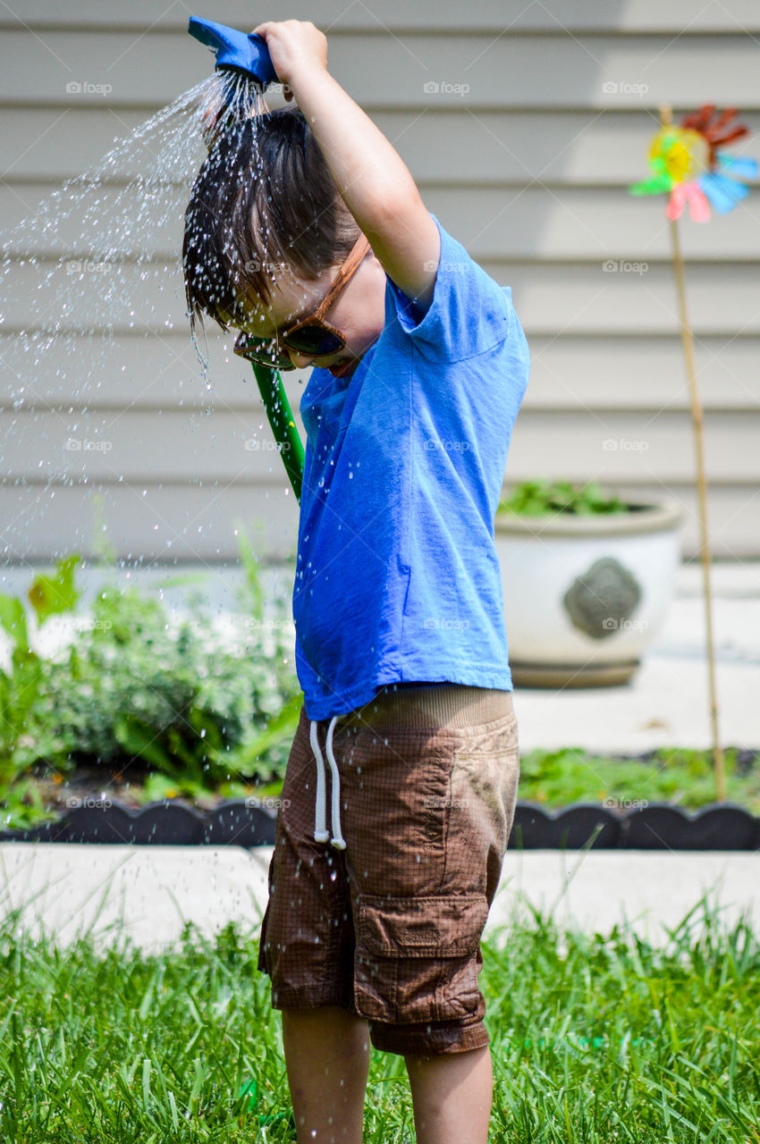 Young boy spraying himself with a garden hose outdoors during summer