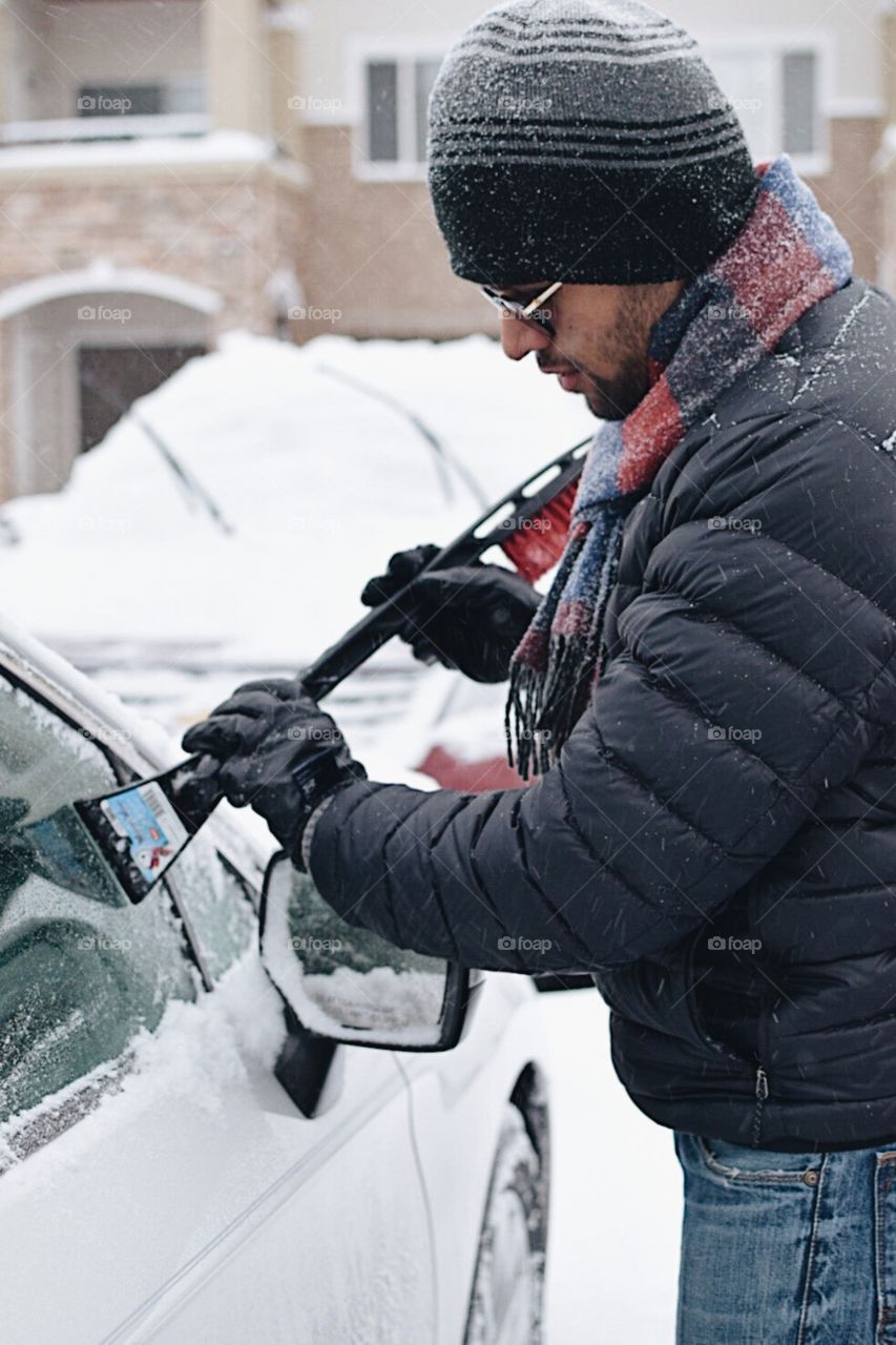 Young man cleaning car in snow 