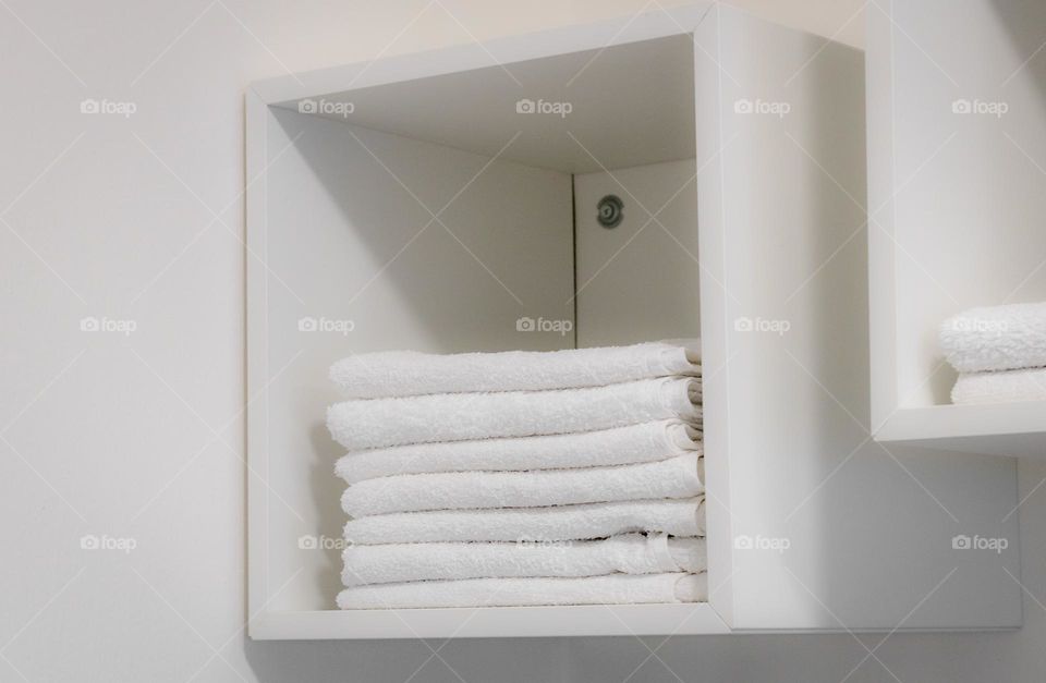 White terry towels folded neatly in a pile lie in a white wall cabinet in a hairdressing salon, close-up side view. The concept of a hairdressing salon, beauty salon.