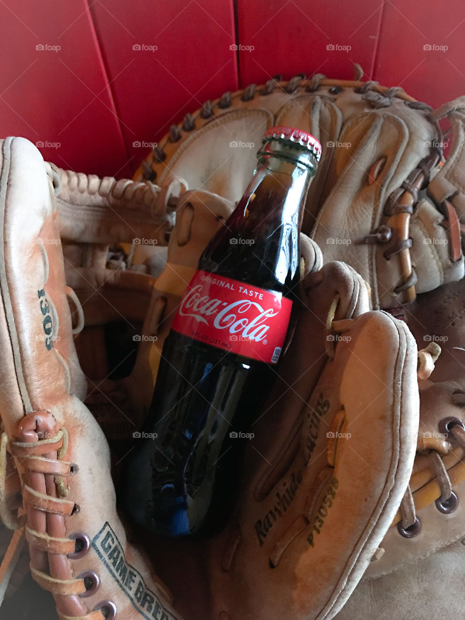 Coke bottle in a baseball glove. Red wooden background. 