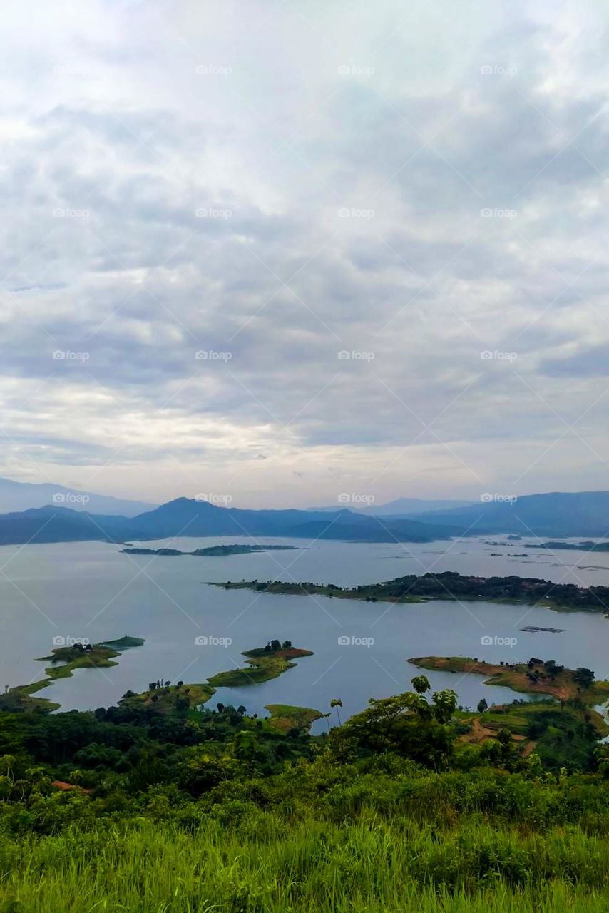 Beautiful natural scenery with a wide lake, small islands, mountains in the distance, and cloudy skies