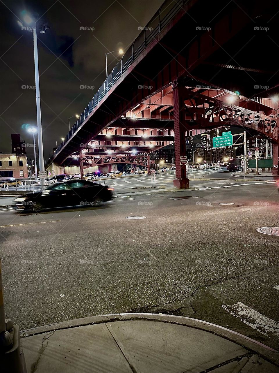 This is the underpass on “Borden Avenue” beneath the “Pulaski Bridge” at “Newtown Creek” in LIC, Queens with spotlight illumination and cars zooming by. 2023. Hypnotic Productions