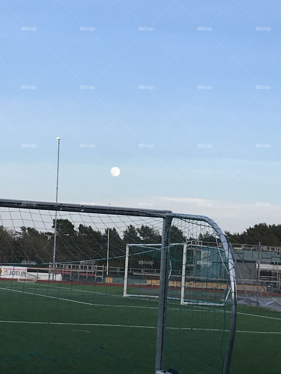 The moon over a football net on a football field. In the evening in the summer with blue skies.