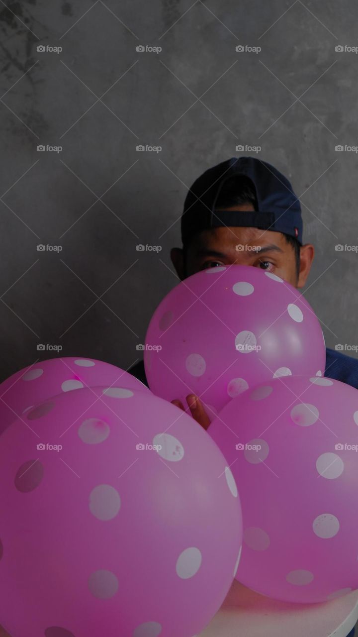 man blowing up a polka dot balloon with his hat turned upside down.