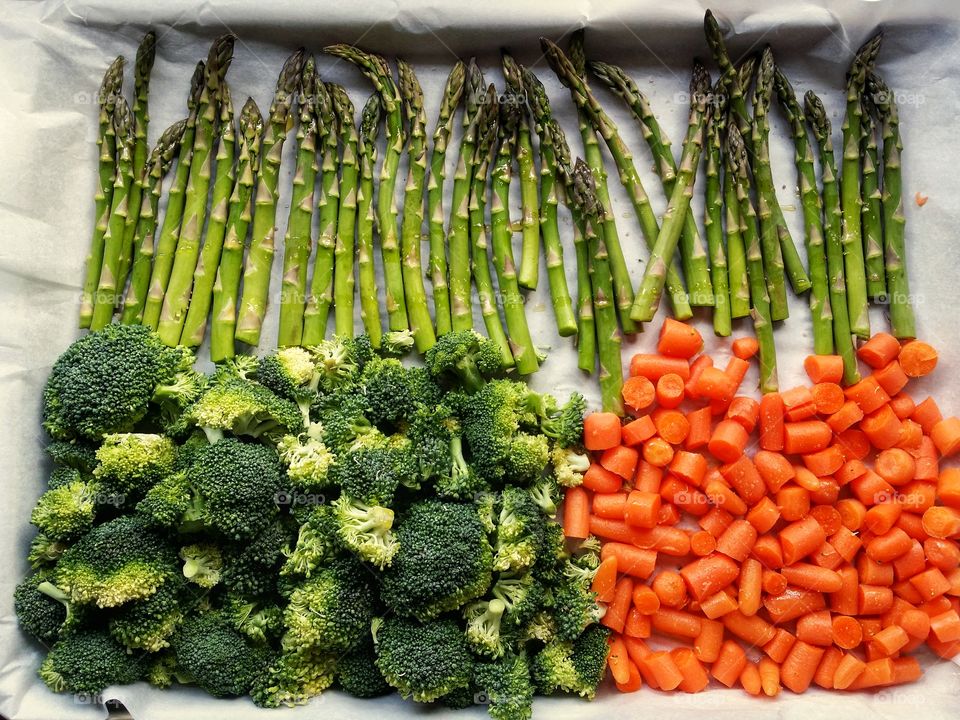 Asparagus broccoli and carrots on a baking sheet with parchment paper drizzled with olive oil and pink salt ready for the oven