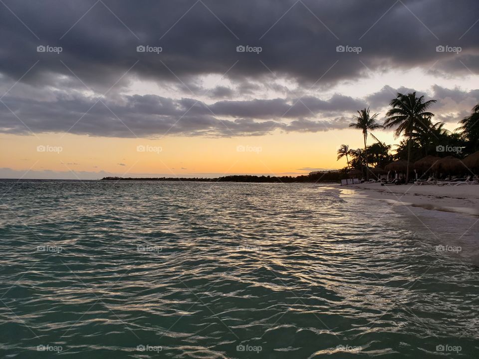 view from swimming in ocean water, beach Shoreline at sunset in Mexico with silhouettes of palm trees