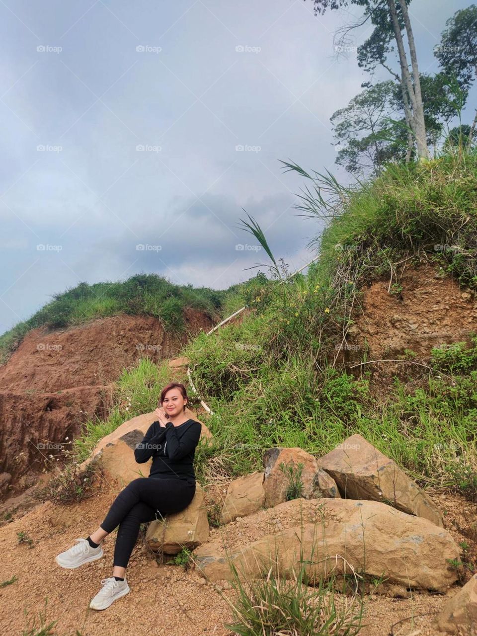 Young woman sitting on a large rock in nature with a background of land, grass and trees