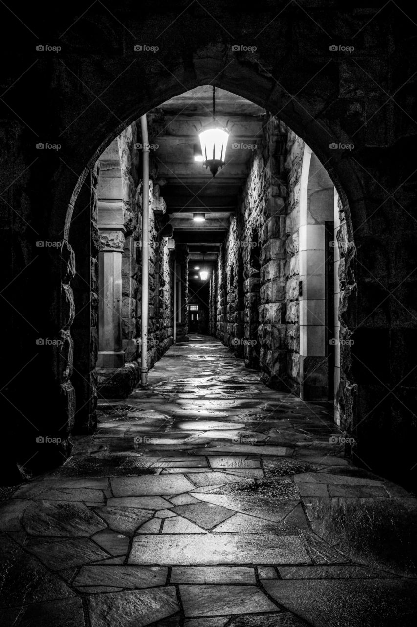 Dark black and white of a gothic style corridor with an arch for an entry at the All Saints Chapel just after an evening rain in Sewanee Tennessee. 