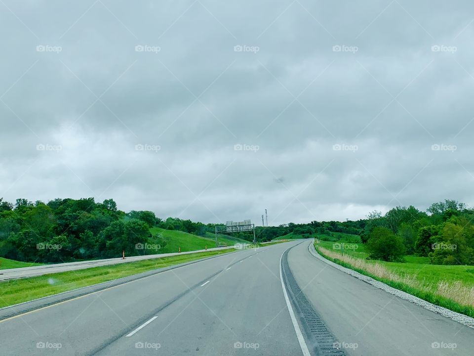 Low-angle view a curving, rural stretch of the interstate with bright green grass and trees on either side under a grey sky in spring 