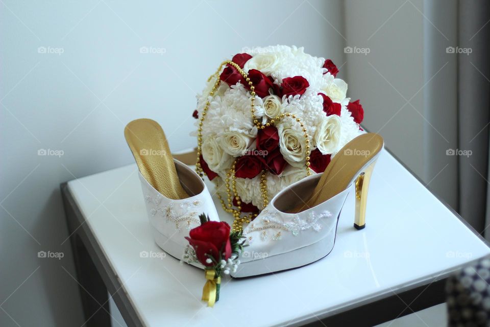 A pair of white women's high heels and a beautiful rose flower bucket.