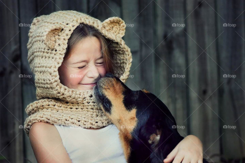 A Young girl squinted as she is playfully loved on by her best friend, her dog.
