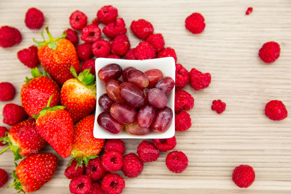 Lay flat image of fresh summer berries on wooden background. Fresh raspberries strawberries and grapes encourage a healthy lifestyle and diet.