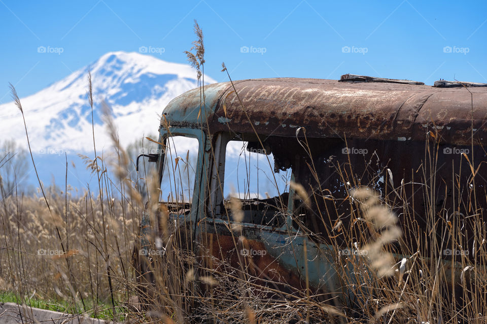 Abandoned and rusty old Soviet Russian bus in the middle of reeds and agriculture fields with snow-capped scenic Ararat mountain and clear blue sky on the background in rural Southern Armenia in Ararat province on 4 April 2017.