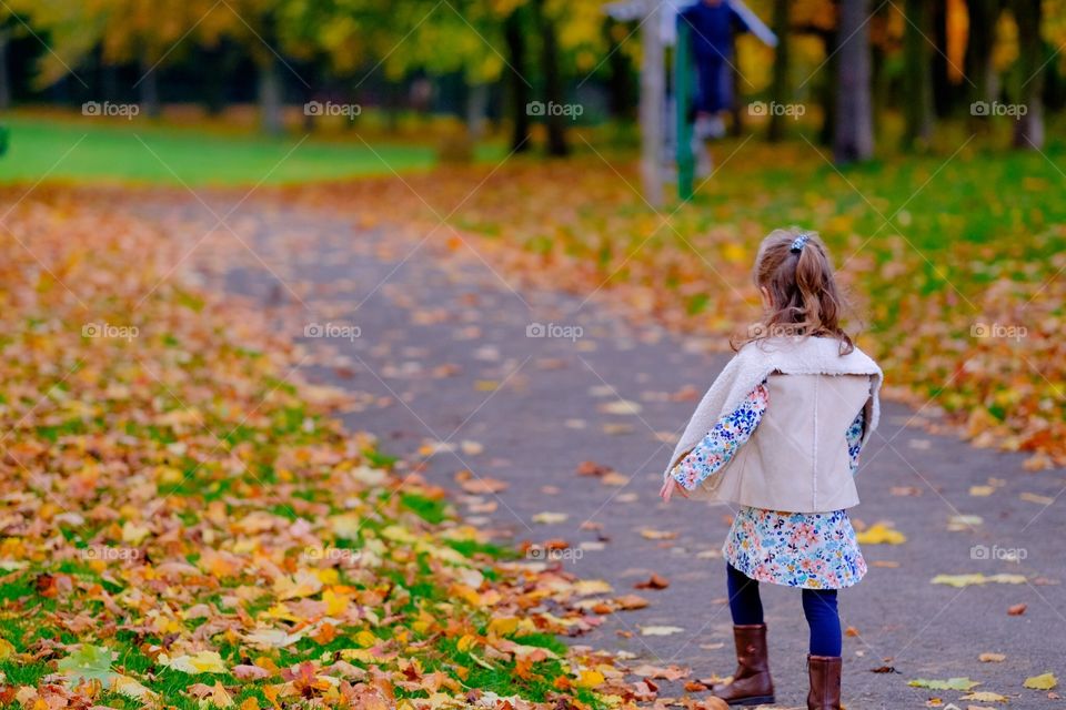 Autumn is child's play. . A young girl, aged three, walks through a park in Autumn with fall colours and a carpet of leaves. 