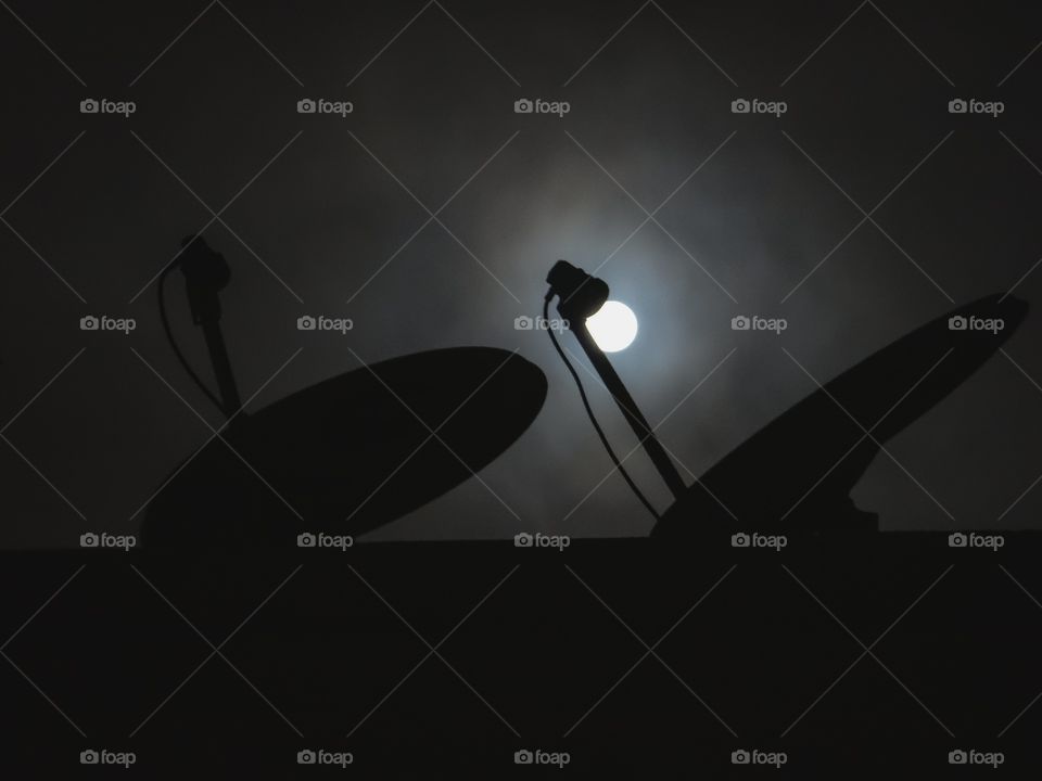 Silhouette of dish tv antennas in the foreground of moon light