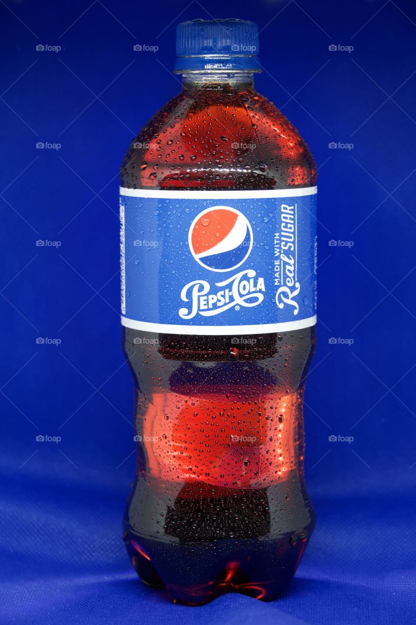 Pepsi bottle backlit with real sugar label against dark blue background.