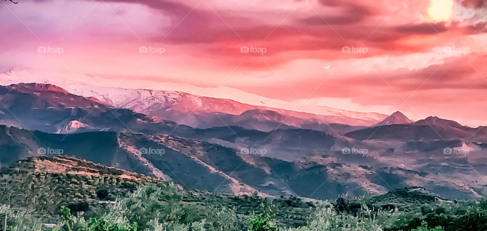 Landscape of mountains near Granada, Spain during a pink and cloudy sunset. The image is soft focus with a slight paint strokes filter applied