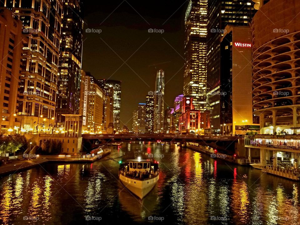 A tourist boat makes its way through downtown Chicago on a warm summer night as amber lights glow