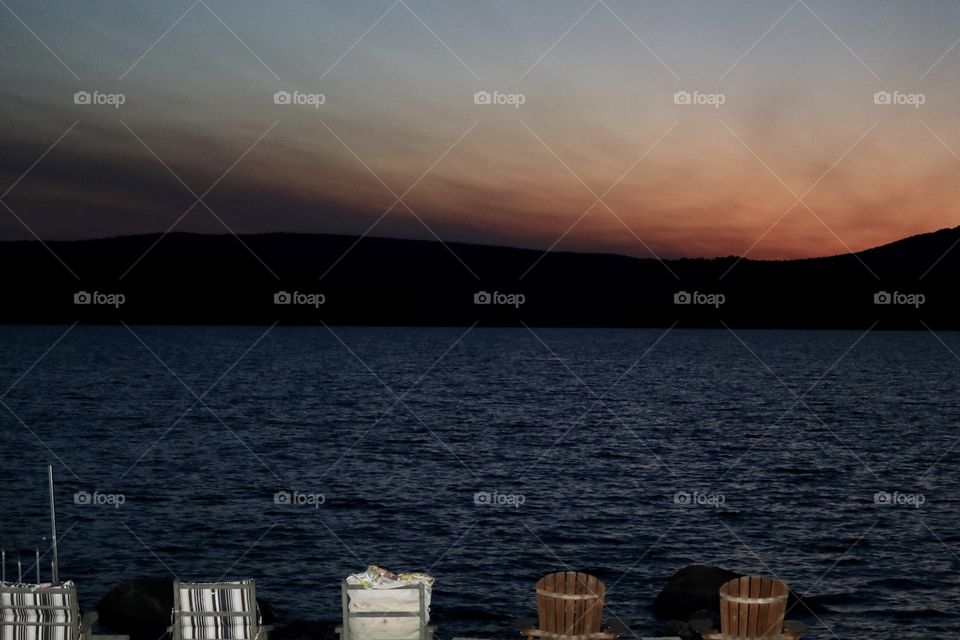 Sunset over an Adirondack mountain lake, backlit Adirondack and lawn chairs