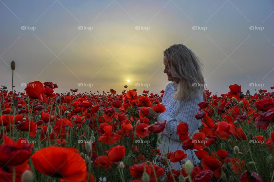 a girl is weaving a wreath in a poppy field
