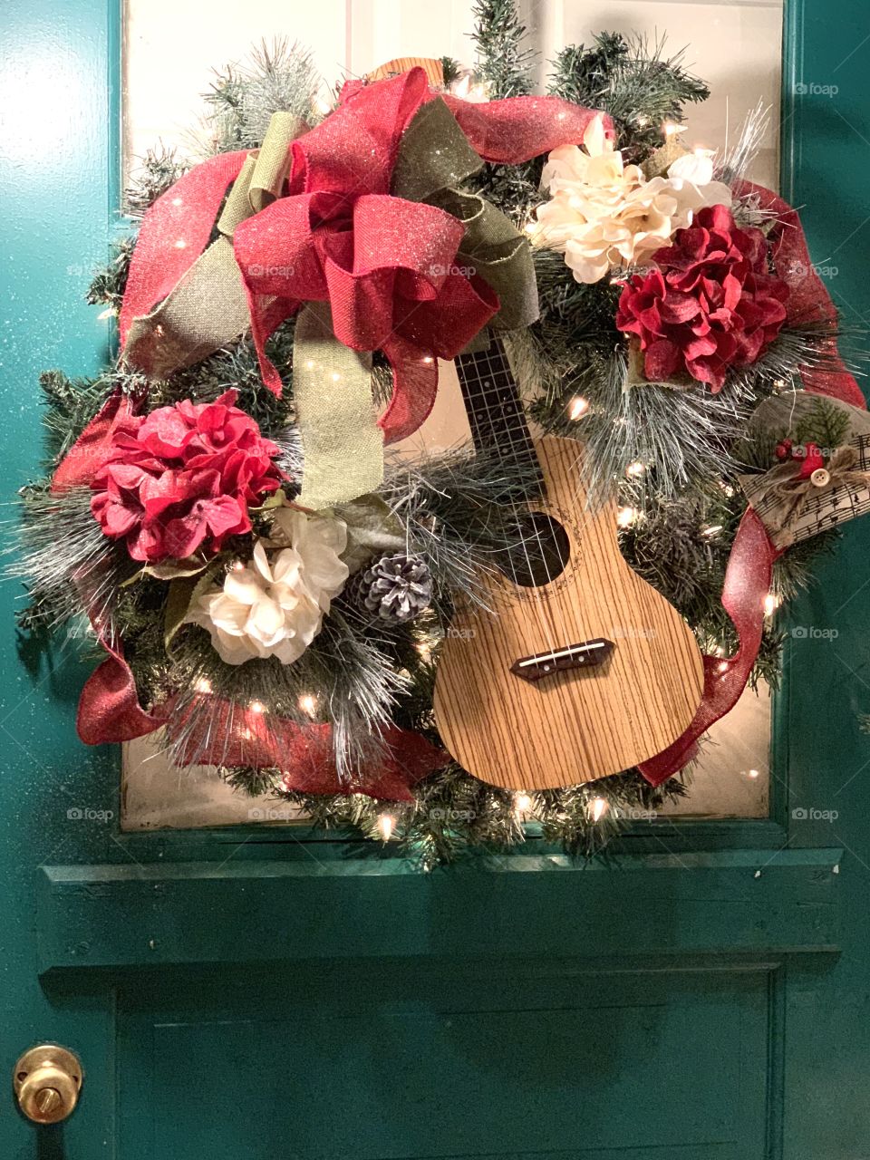 Festive Christmas Wreath on Front Door with red ribbon, musical instrument of a guitar, lights, flowers, pine needles 