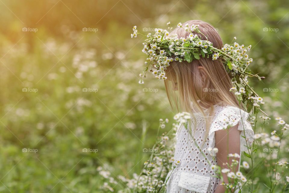 Little girl with camomile wreath in countryside 