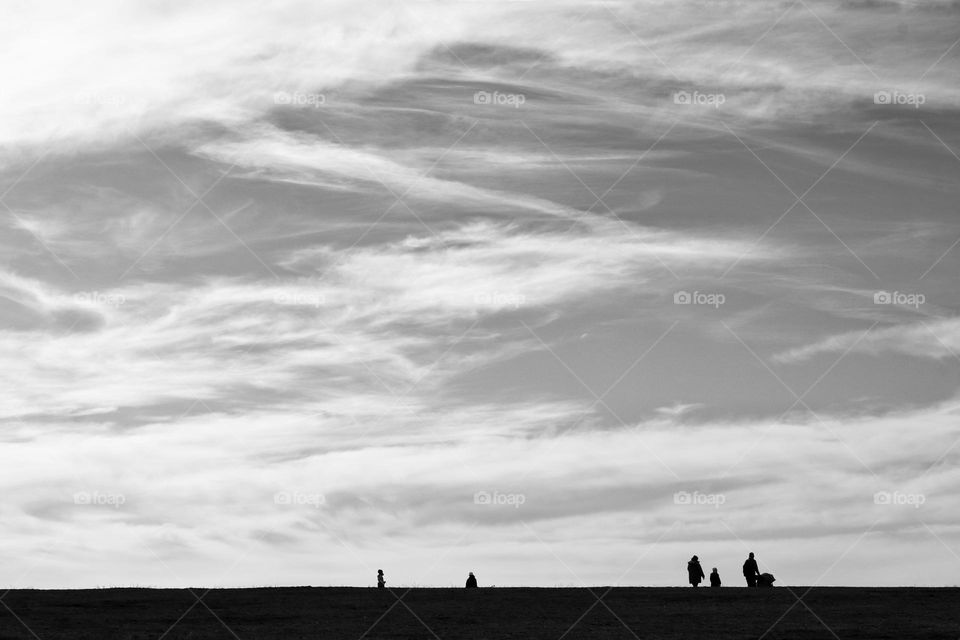 Black and white photos of the silhouette of people walking on the horizon under sky with veiled clouds