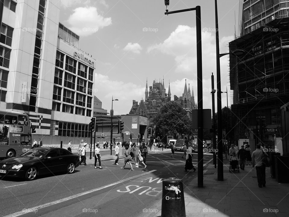 People walking and vehicles moving and parked on a busy ornate building lined buildings with shops on a busy street in London on a sunny summer day. 