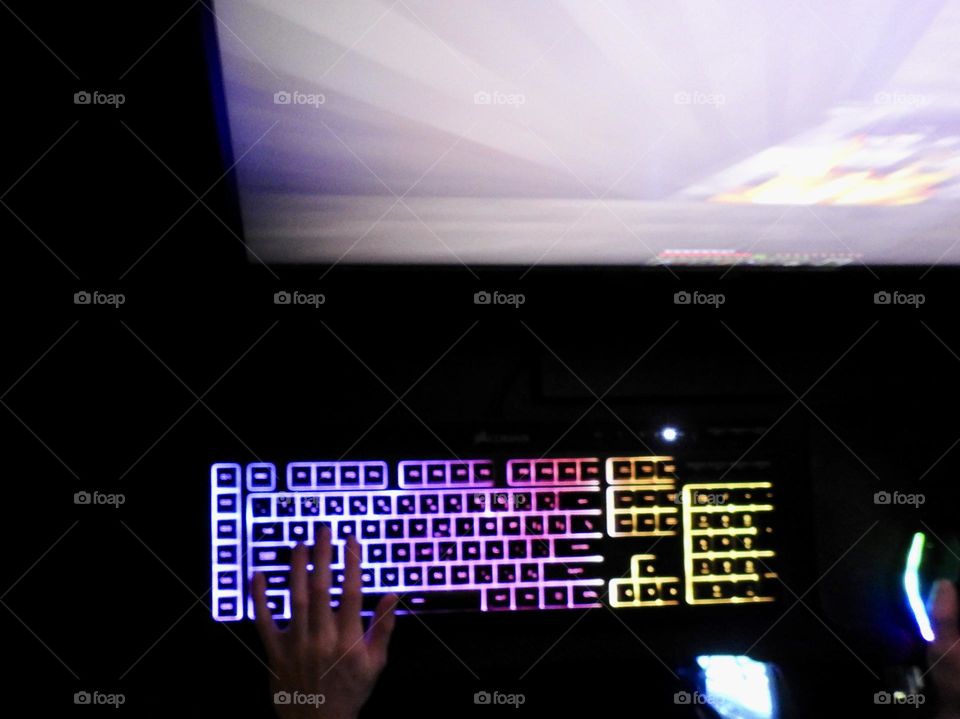 Teenager boy playing Minecraft on the gaming computer seen from a high angle and seeing his hand playing using the keyboard and the mouse accessories in a dark room.