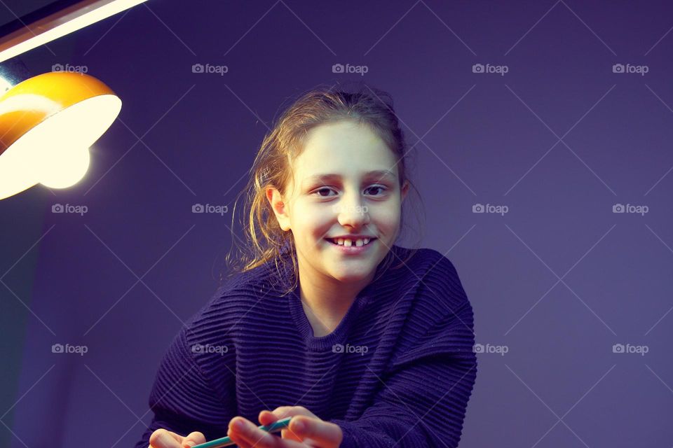 the girl is doing her homework and is distracted smiling at the camera. purple background